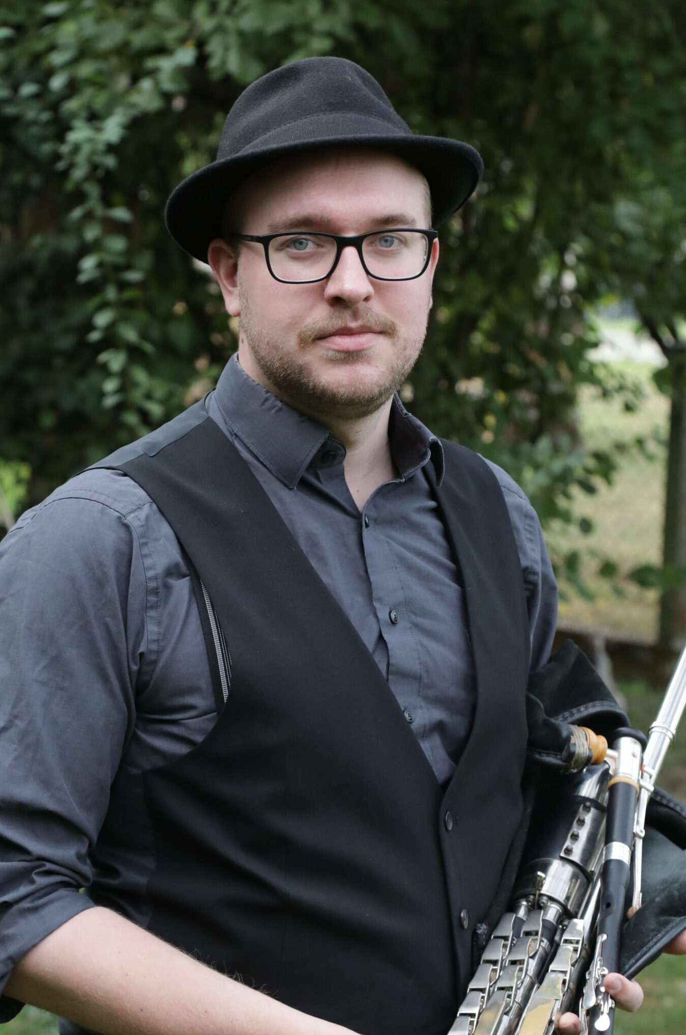 well dressed man with dark clothes holding irish uilleann bagpipes